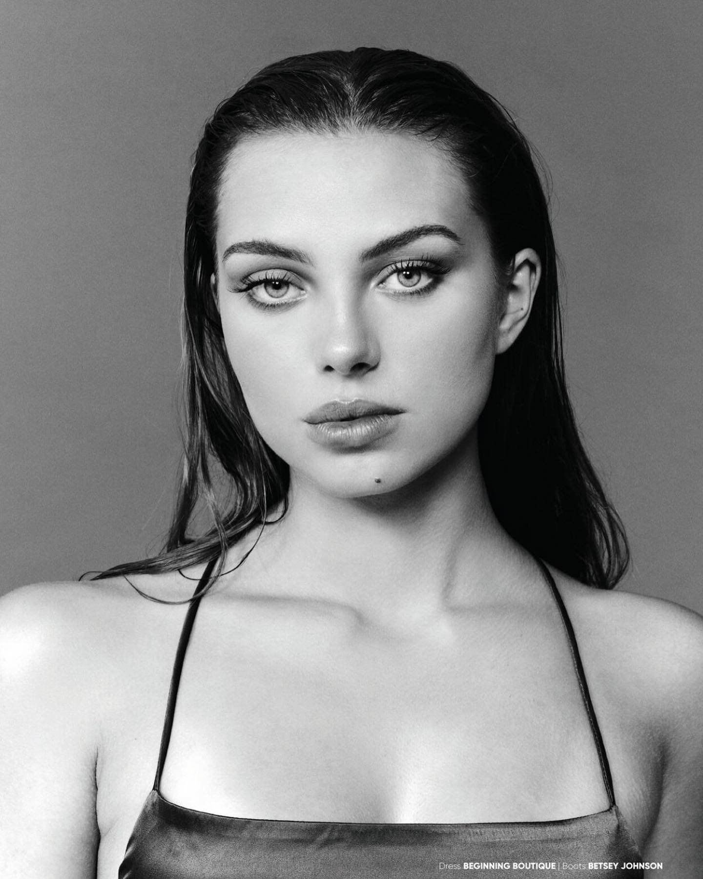 Black and white portrait of a young woman with wet hair, wearing a sleek satin top. The photo highlights her facial features.