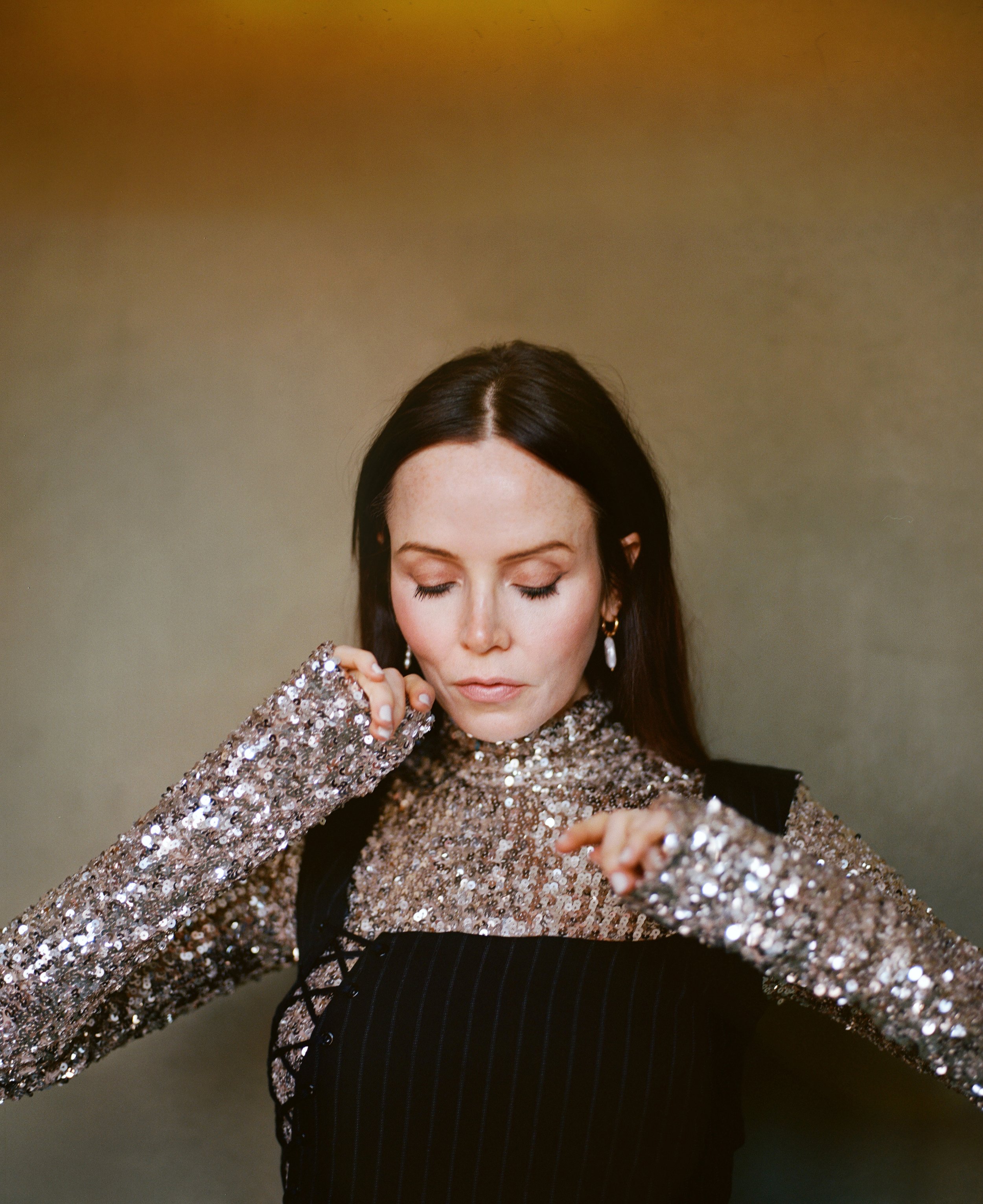 Close-up portrait of a woman wearing a sparkling sequin top and a black laced garment, styled by Corina Gaffey.
