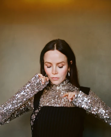 Close-up portrait of a woman wearing a sparkling sequin top and a black laced garment, styled by Corina Gaffey.