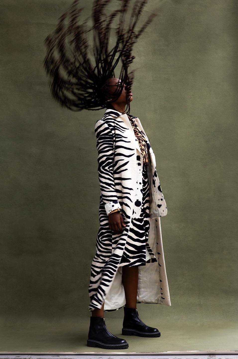 A woman wearing a white and black zebra-print coat and dress stands in a photo studio while whipping her long hair.