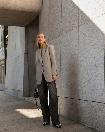 Stylish woman in an oversized blazer and sparkling pants stands in an urban setting with natural light highlighting her outfit.