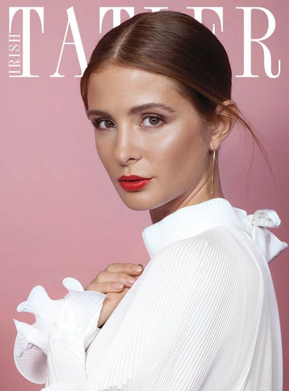 Close-up of a brunette adult female model in a white ruffled top with red lipstick against a pink background for a magazine cover.