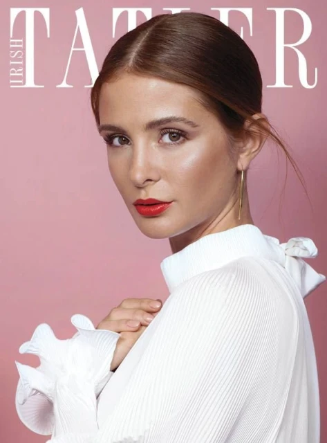 Close-up of a brunette adult female model in a white ruffled top with red lipstick against a pink background for a magazine cover.