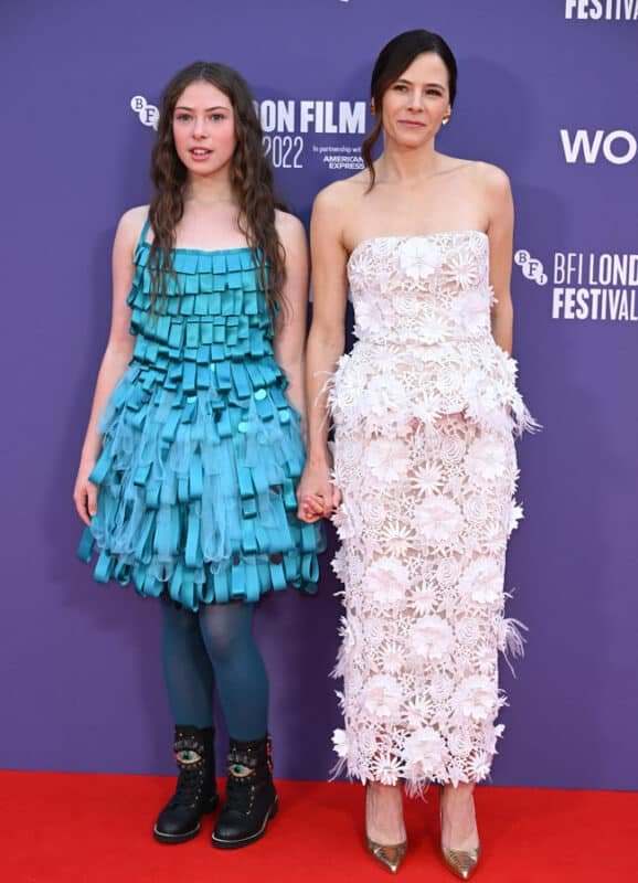 A young girl in a blue dress and an adult woman in a white dress pose on a red carpet at the BFI London Film Festival 2022.