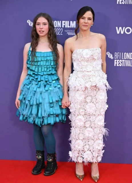 A young girl in a blue dress and an adult woman in a white dress pose on a red carpet at the BFI London Film Festival 2022.