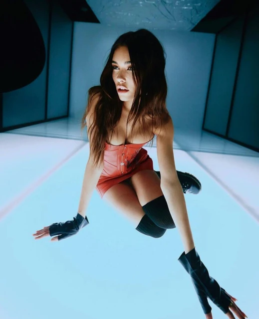 A fashionable young woman in a corset and fingerless gloves poses indoors against a blue and white geometric background in a dramatic shot.