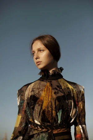 Portrait of a woman wearing a patterned ruffled blouse against a clear blue sky, styled by Corina Gaffey.