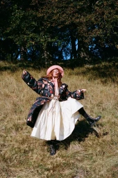 Woman in floral puffer jacket and white dress posing on grassy hill styled by Corina Gaffey