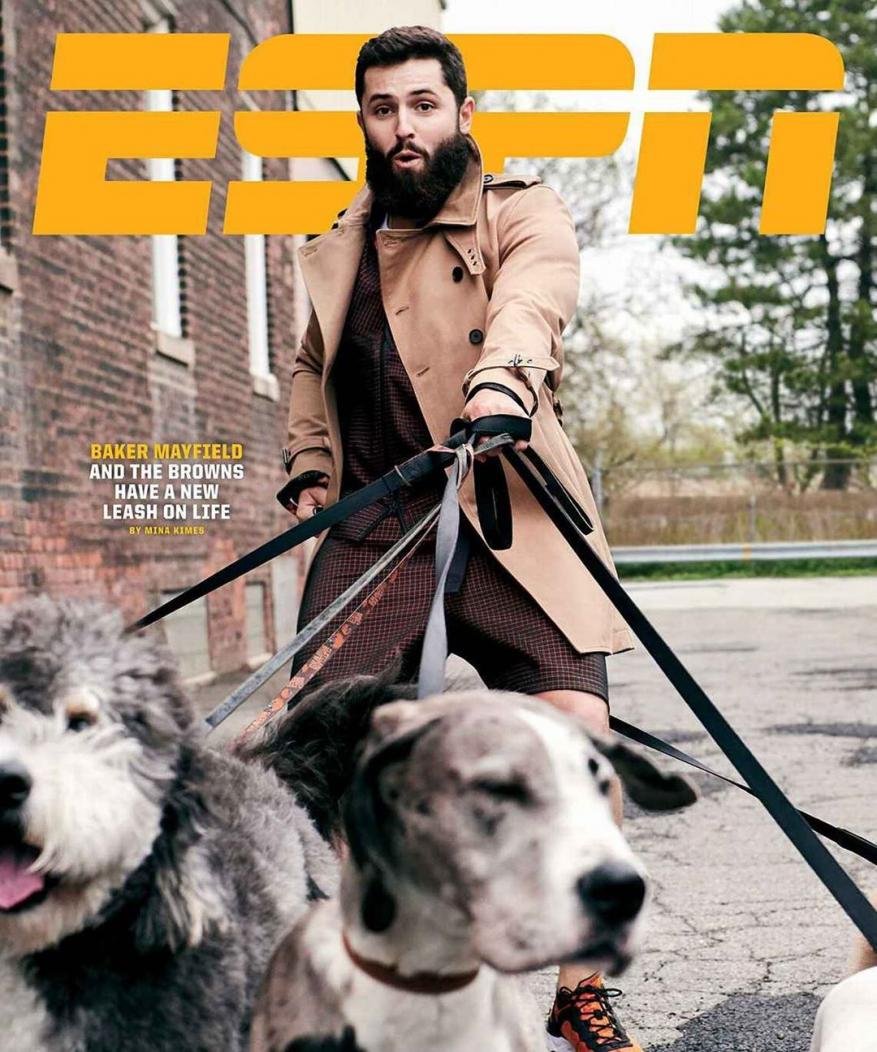 Magazine cover featuring an adult man wearing a trench coat walking two dogs on leashes outdoors near a brick building.