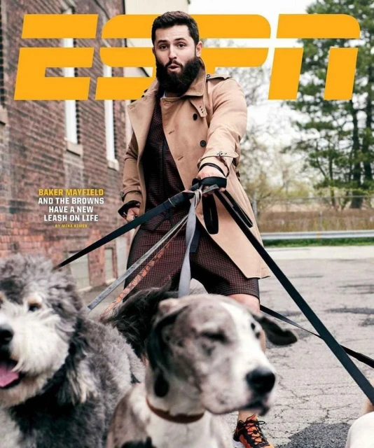 Magazine cover featuring an adult man wearing a trench coat walking two dogs on leashes outdoors near a brick building.