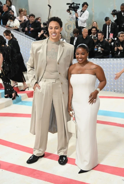 Brittney Griner and her wife, Cherelle Griner, pose together on a decorative surface; both wearing light-colored attire, red carpet event.