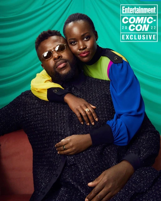 Man and woman pose together in front of a green curtain backdrop, with the 'Entertainment Comic-Con 2022 Exclusive' logo visible.