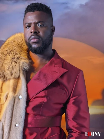 Portrait of a bearded man in a red suit jacket with a fur coat against a blurred sunset background. Fashion and style.