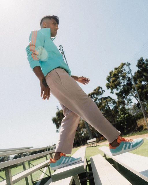 A stylish man wearing a blue Adidas track jacket and pants poses on bleachers, showcasing the brand's sporty aesthetic and urban style.