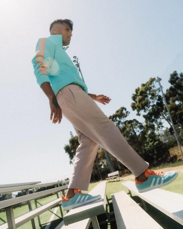 A stylish man wearing a blue Adidas track jacket and pants poses on bleachers, showcasing the brand's sporty aesthetic and urban style.