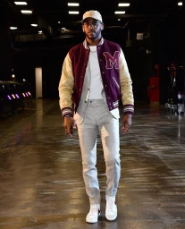 Man wearing a maroon varsity jacket, light grey trousers, white t-shirt, and cap walking indoors.