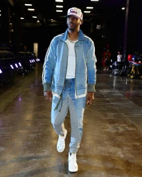 Chris Paul wearing a denim jacket and grey trousers walks indoors in Los Angeles styled by Courtney Mays.