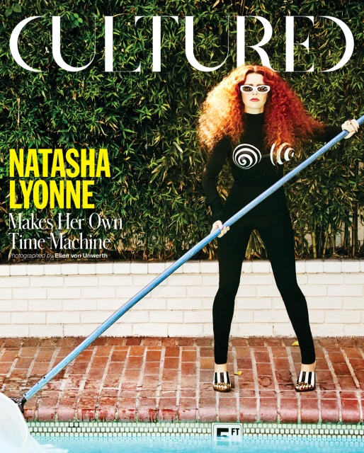 Magazine cover of Natasha Lyonne holding pool skimmer in black bodysuit with circular designs, white sunglasses, red curly hair, near pool.