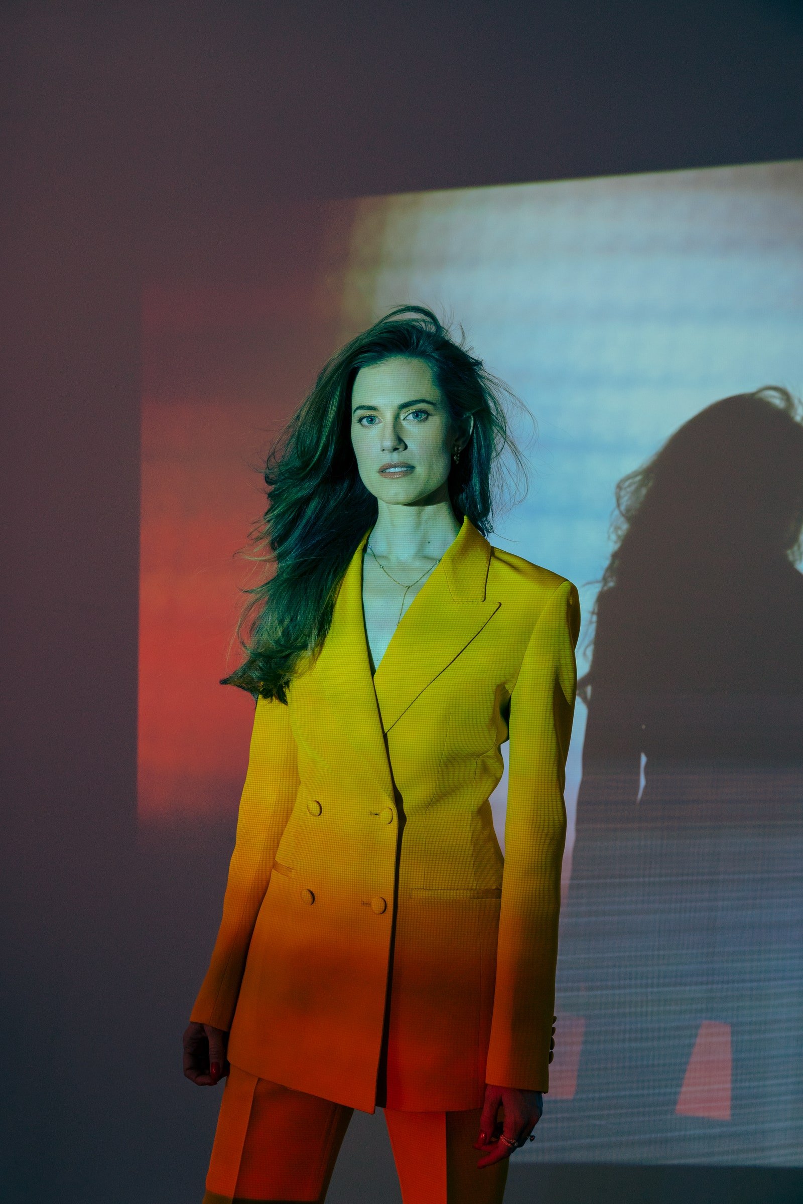 Woman wearing a bright yellow double-breasted suit jacket with projection lighting on a plain background