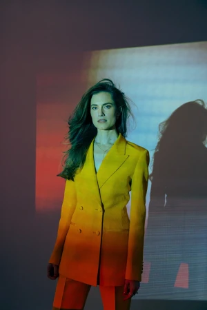 Woman wearing a bright yellow double-breasted suit jacket with projection lighting on a plain background