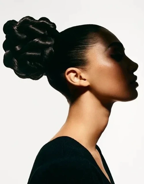 Profile shot of a dark-haired woman with a high bun hairstyle, wearing a black top, set against a bright white studio backdrop.