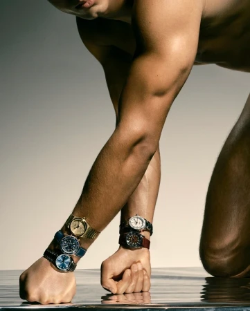 Close-up portrait of a man wearing multiple wristwatches while leaning forward against a reflective studio backdrop in London.