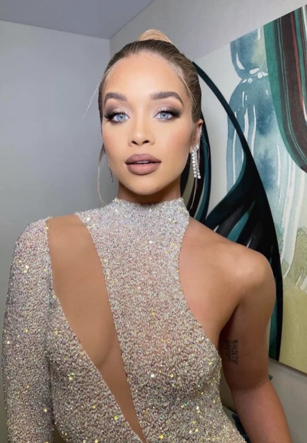 Close-up portrait of a woman with light skin, blue eyes, and her blonde hair in a bun, wearing a sparkly dress against a light background.