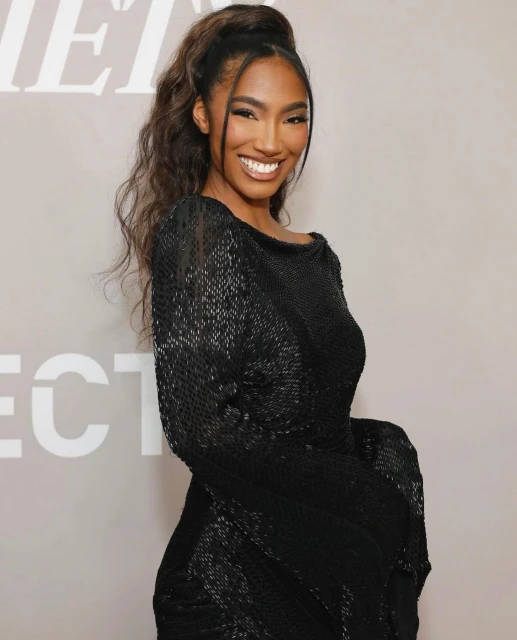 Portrait of a smiling woman with dark hair in a black sequin dress in front of a grey background with white block letters.
