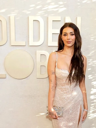 Woman in a beaded evening gown holding a small metallic clutch against a textured wall with large lettering.