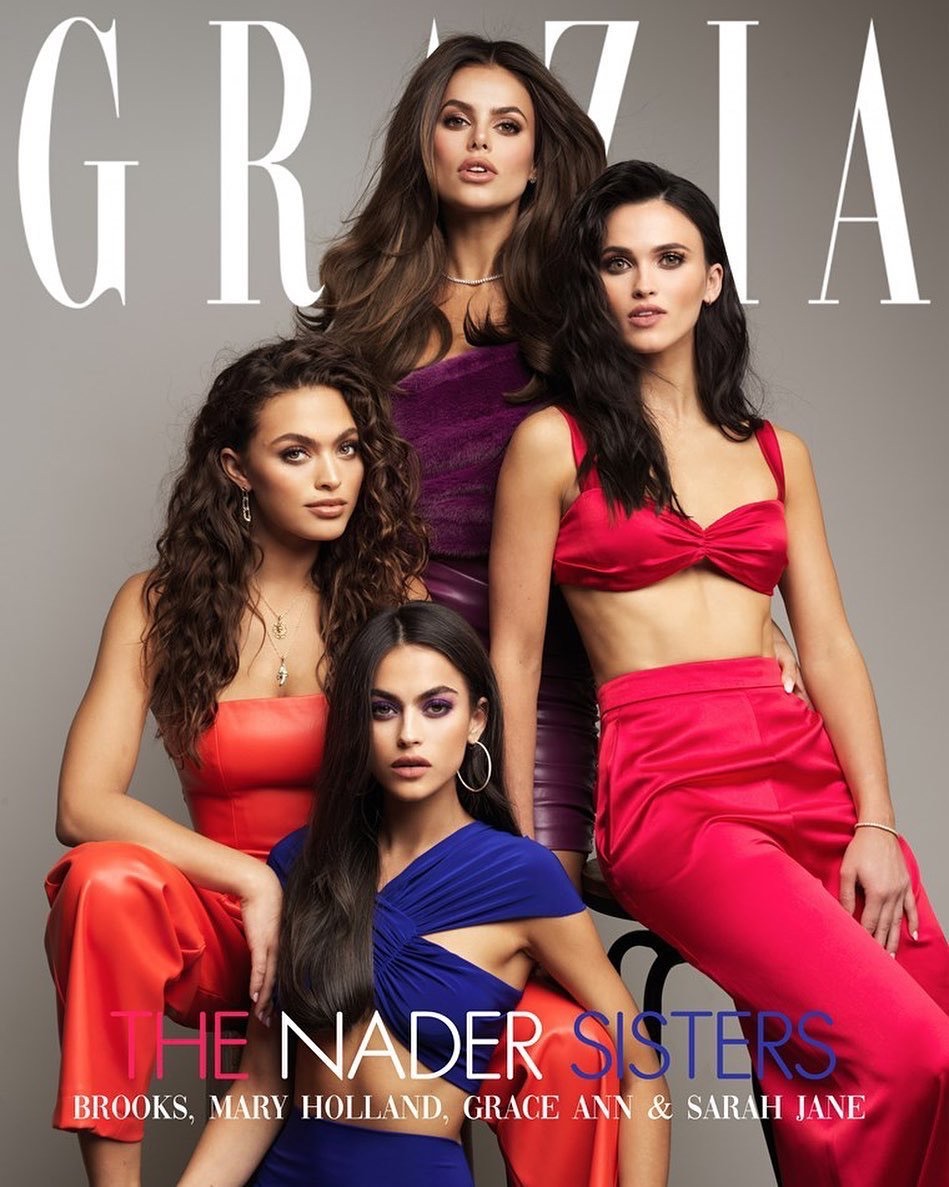 Four adult women are posing in a photo studio setting, wearing colorful coordinated outfits, for a magazine cover shoot. The women have neutral facial expressions.