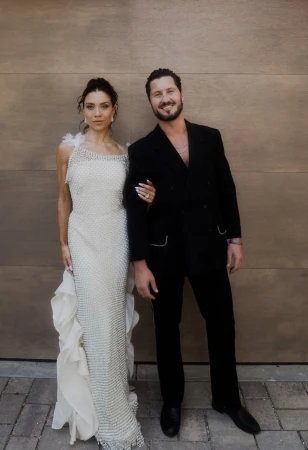 An adult couple is standing together posing for a portrait; the adult female is in a beaded gown and the adult male in a black suit.