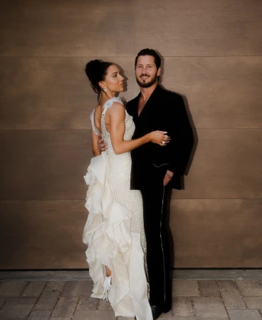 A man in a black suit and a woman in a white embellished gown posing against a wood-paneled wall styled by Danielle Alix