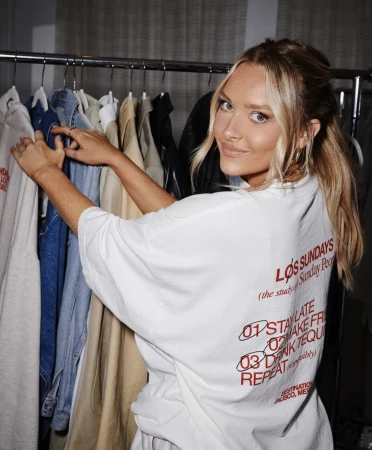 Blonde woman in a white t-shirt reaching for garments on a clothing rack filled with denim jackets and coats.