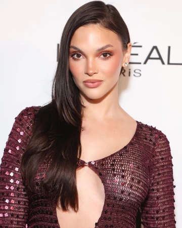 Portrait of a woman with long dark hair wearing a maroon sequin dress against a branded backdrop styled by Danielle Alix.