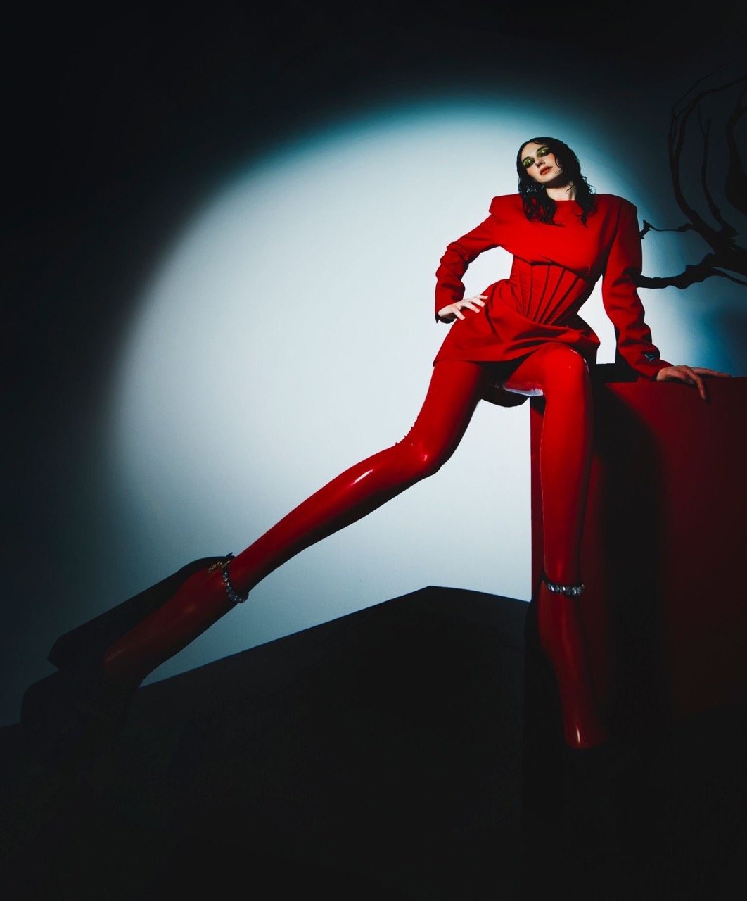 Fashion model in vibrant red corset-style outfit strikes a pose against a gradient light and shadow backdrop in a studio setting.