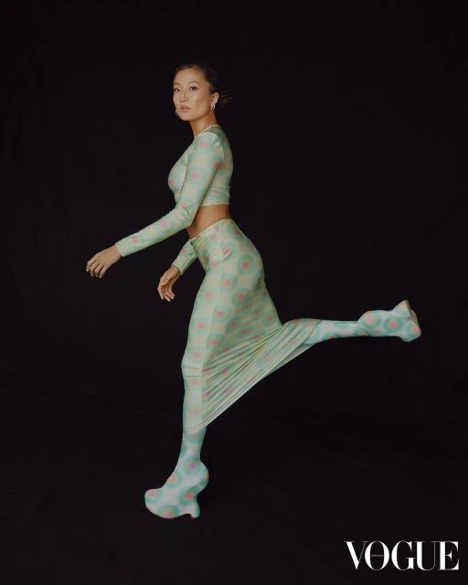 Portrait of an Asian woman in a patterned two-piece outfit striking a dynamic pose against a dark background, showcasing fashion and style.