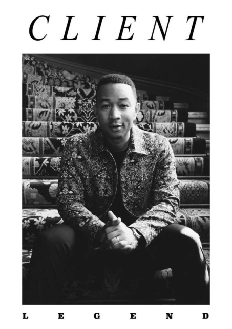 Black and white portrait of a man sitting on a staircase with a patterned carpet in a magazine cover style, showcasing fashion and design.