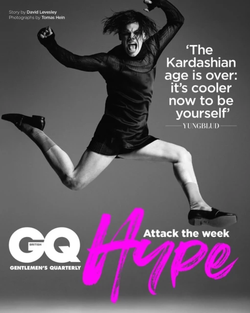 Magazine cover featuring a man in mid-air, arms raised, with an open mouth expression, wearing a black dress and shoes against a gray background.
