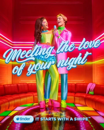 A woman and a man stand on a disco ball, singing into a microphone in a retro-themed room with neon lights and orange seating.