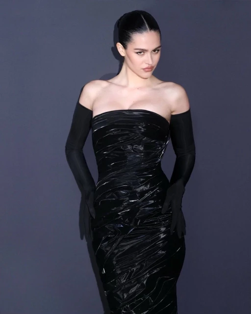 Woman poses in black strapless dress with opera gloves against a neutral backdrop, emphasizing fashion and elegant presentation.