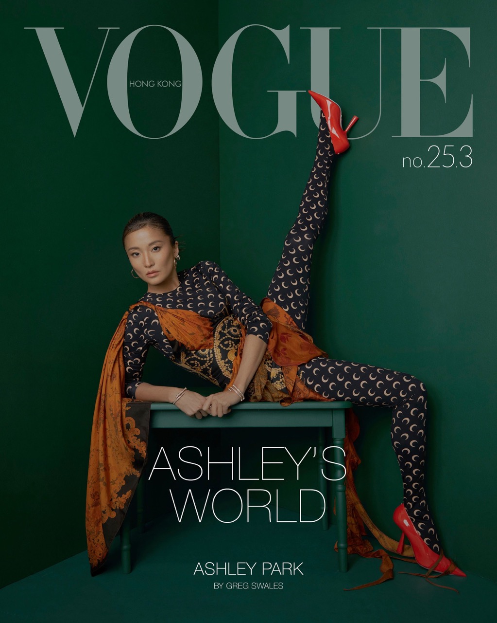Magazine cover featuring a woman in patterned leggings and heels, seated on a table against a dark green backdrop, Vogue Hong Kong.