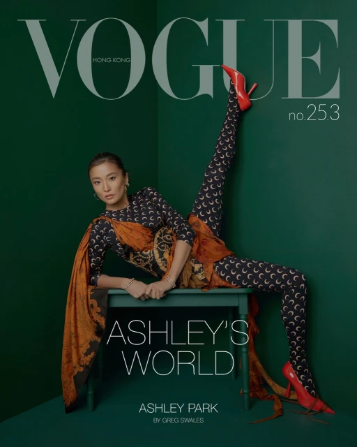 Magazine cover featuring a woman in patterned leggings and heels, seated on a table against a dark green backdrop, Vogue Hong Kong.