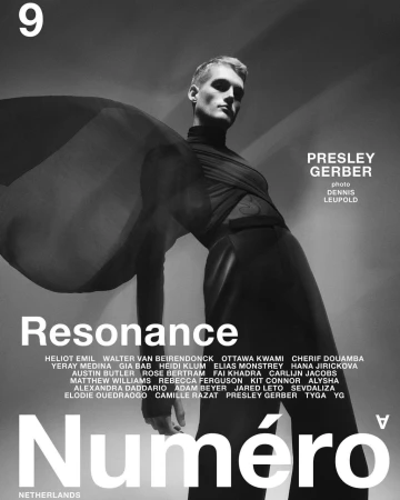 Black and white fashion editorial shot of a male model wearing a black turtleneck and draped fabric, posing in front of a gradient backdrop.