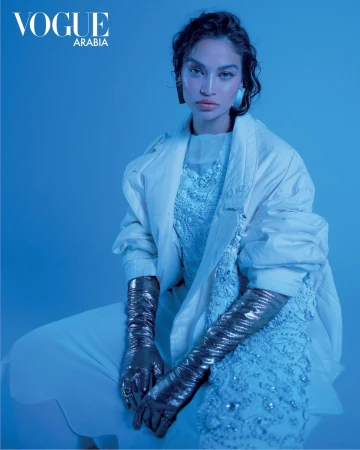 Model in white layered outfit wearing shiny metallic gloves under intense blue lighting for Vogue Arabia editorial