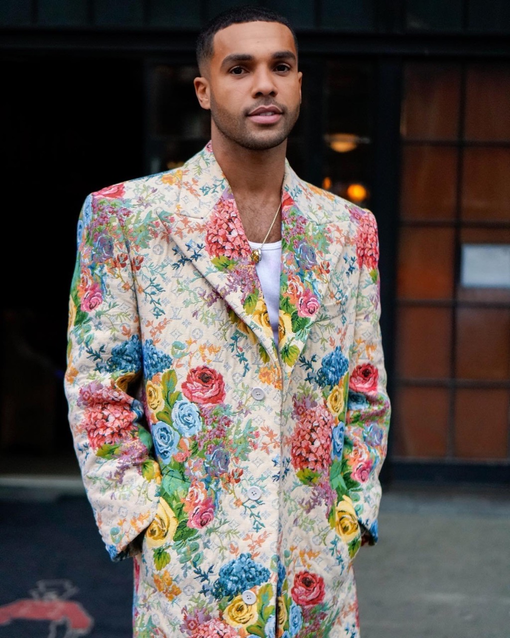 A stylish man poses outdoors in a floral blazer, showcasing a blend of fashion and nature-inspired design with natural light.