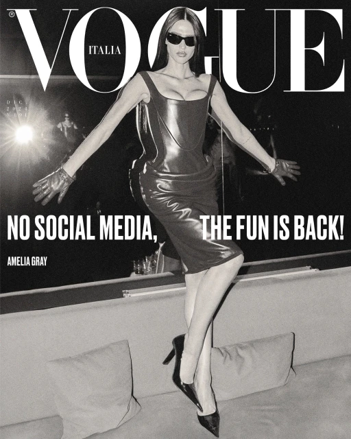 Vogue Italia cover featuring Amelia Gray in a shiny black dress, high heels, and sunglasses striking a pose with outstretched arms.