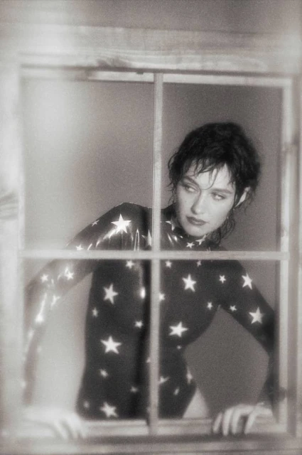 Monochrome portrait of a woman with short hair and a star-patterned bodysuit looking out of a window in a vintage style.