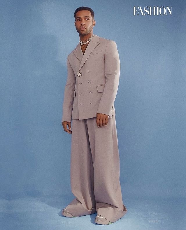 Man wearing a tailored lavender double-breasted suit and wide trousers against a blue background