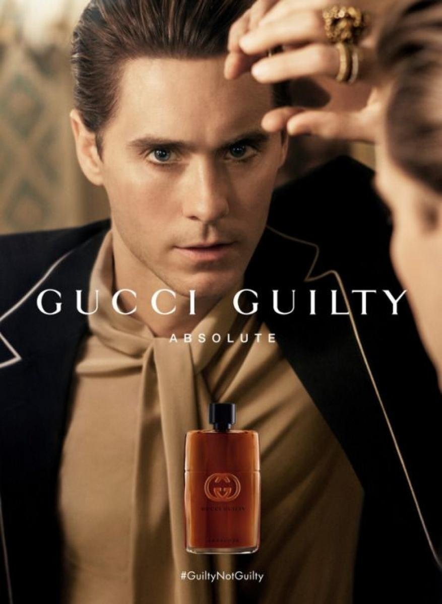Jared Leto in Gucci Guilty advertisement, wearing a jacket, beige shirt, with a bottle of perfume. Close-up shot, studio lighting.