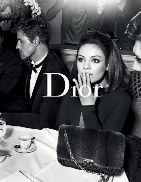 Black and white fashion shot of woman in black dress with fur purse, and man in tuxedo at table with drinks for a Dior ad.
